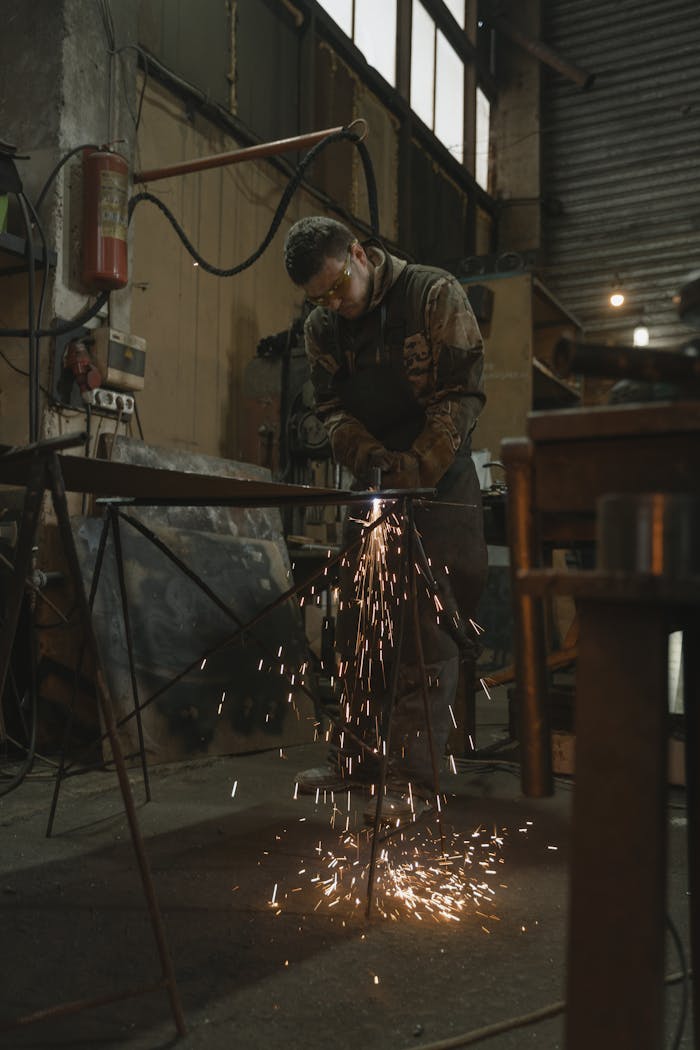 A welder wearing safety glasses works in a factory producing sparks.